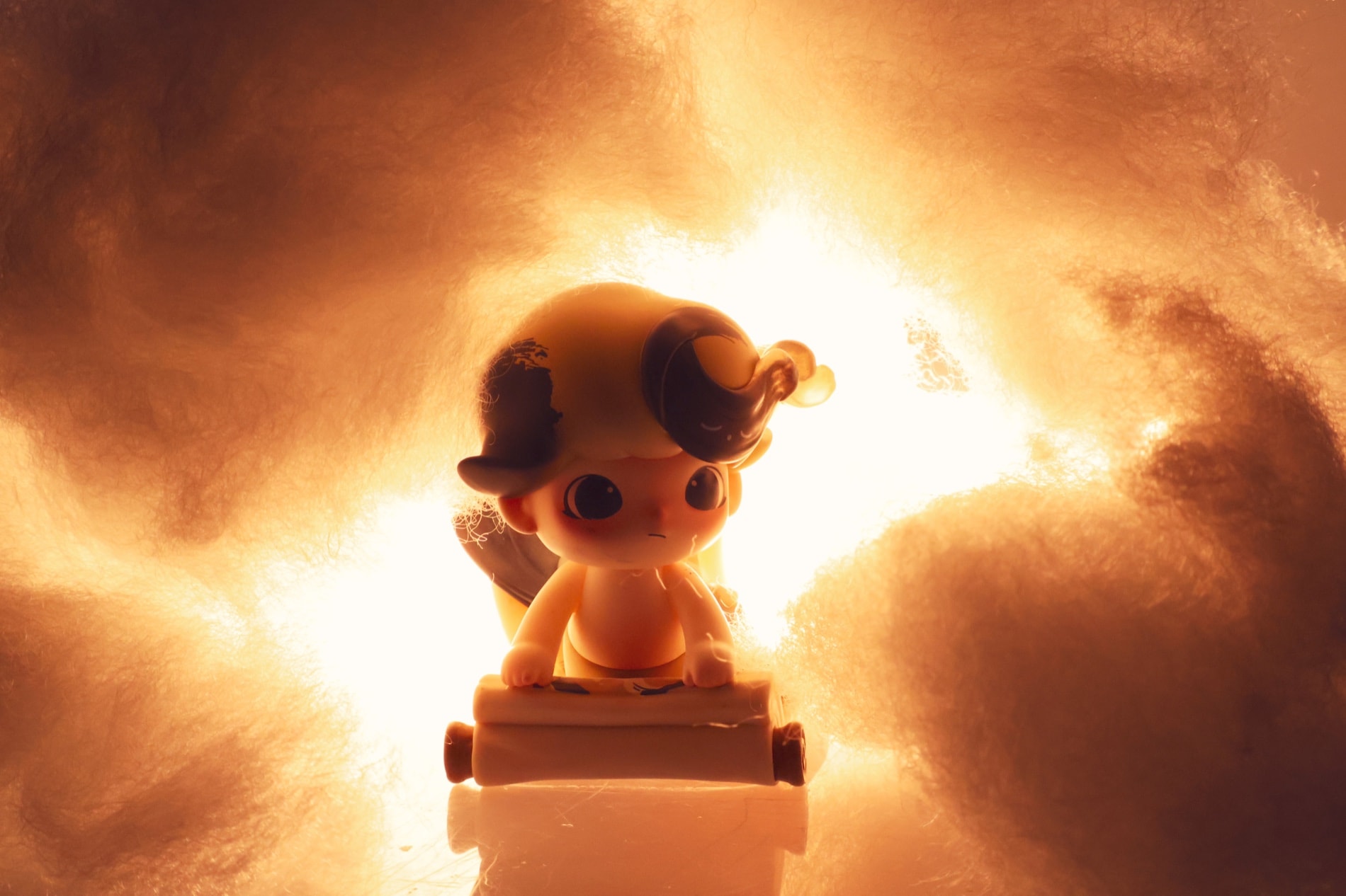 A small vinyl figure holding a scroll, lit from behind through banks of cotton wool
