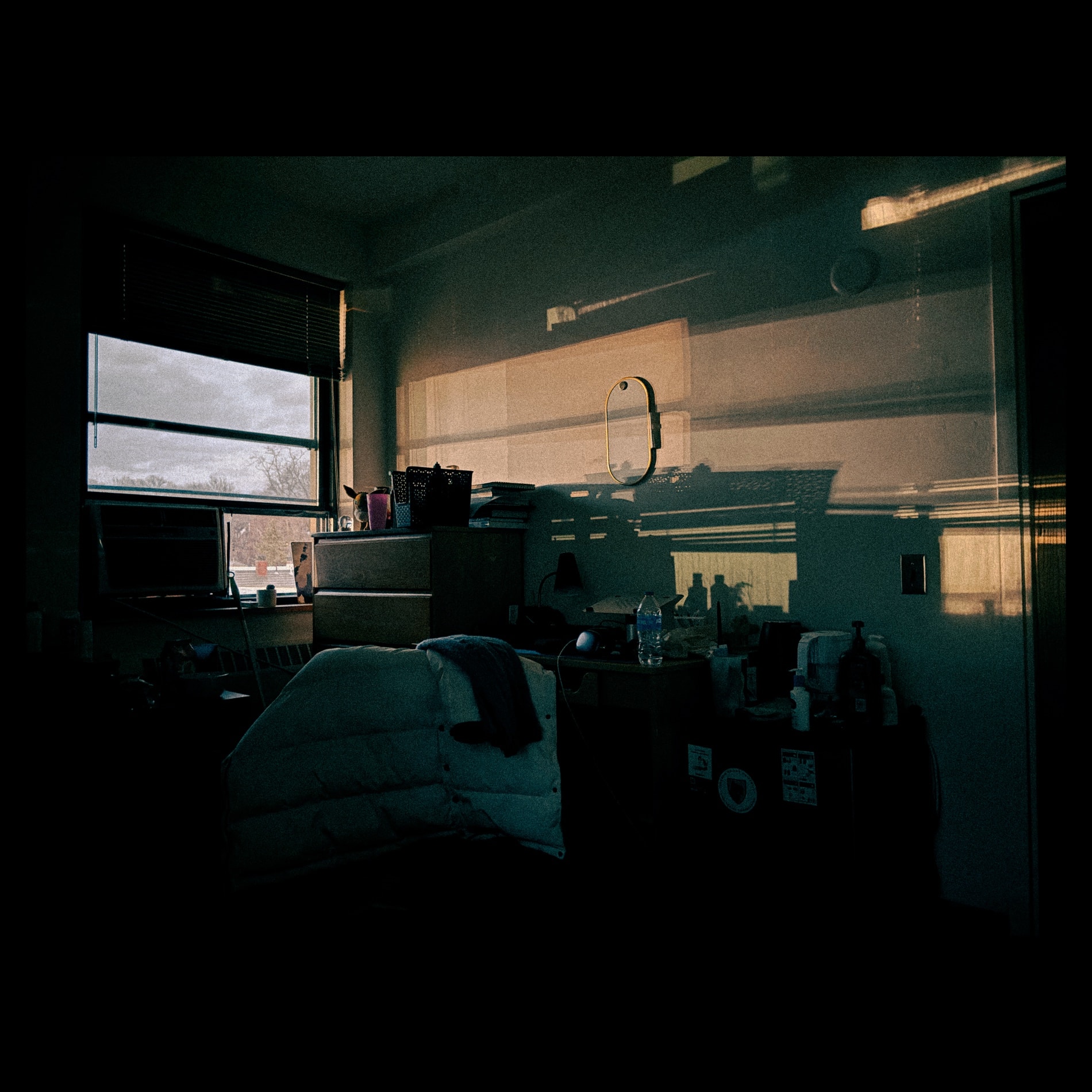 A dark dorm room with a long streak of late sun reflected across the wall