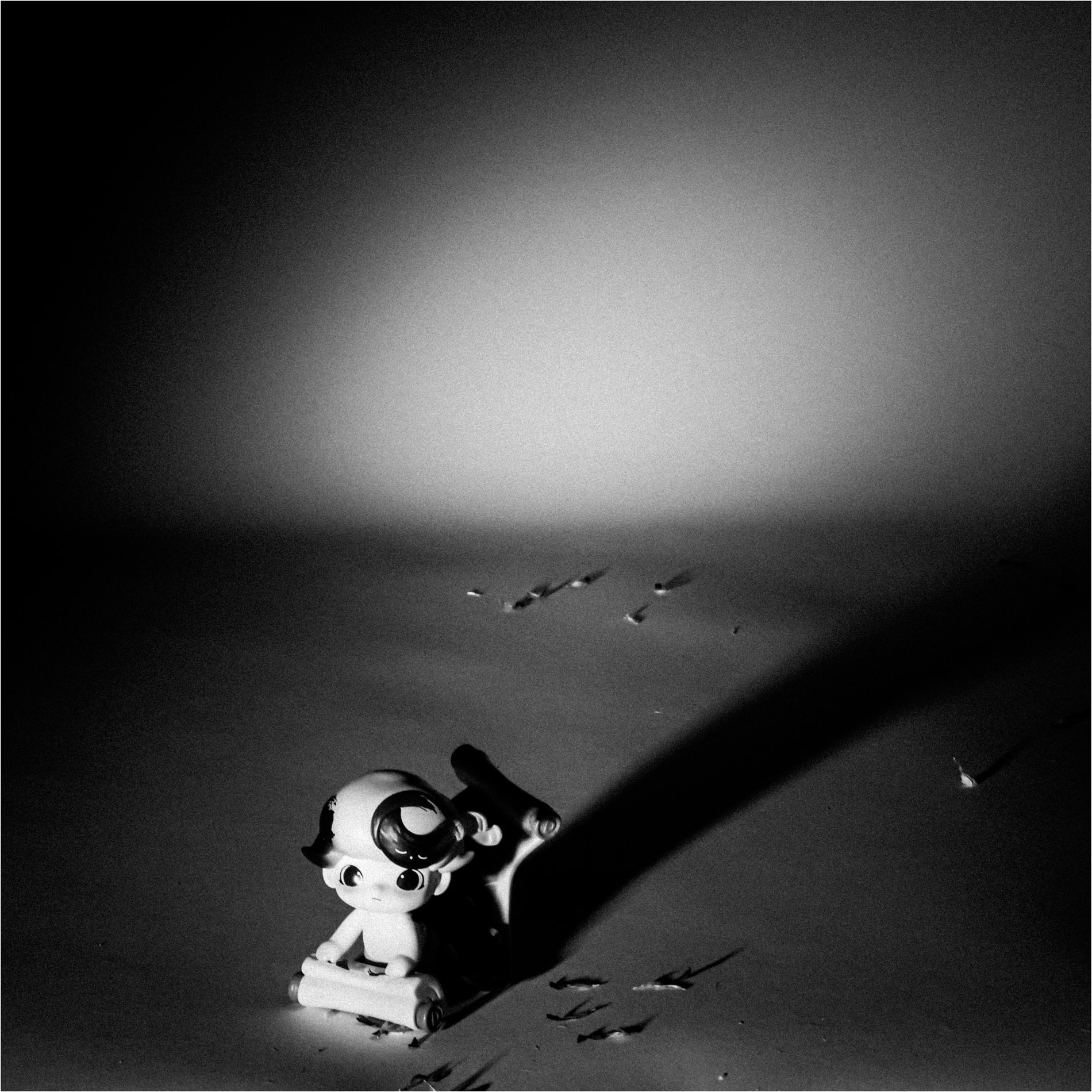 A small figure on a lit plane throwing a long shadow, in black and white