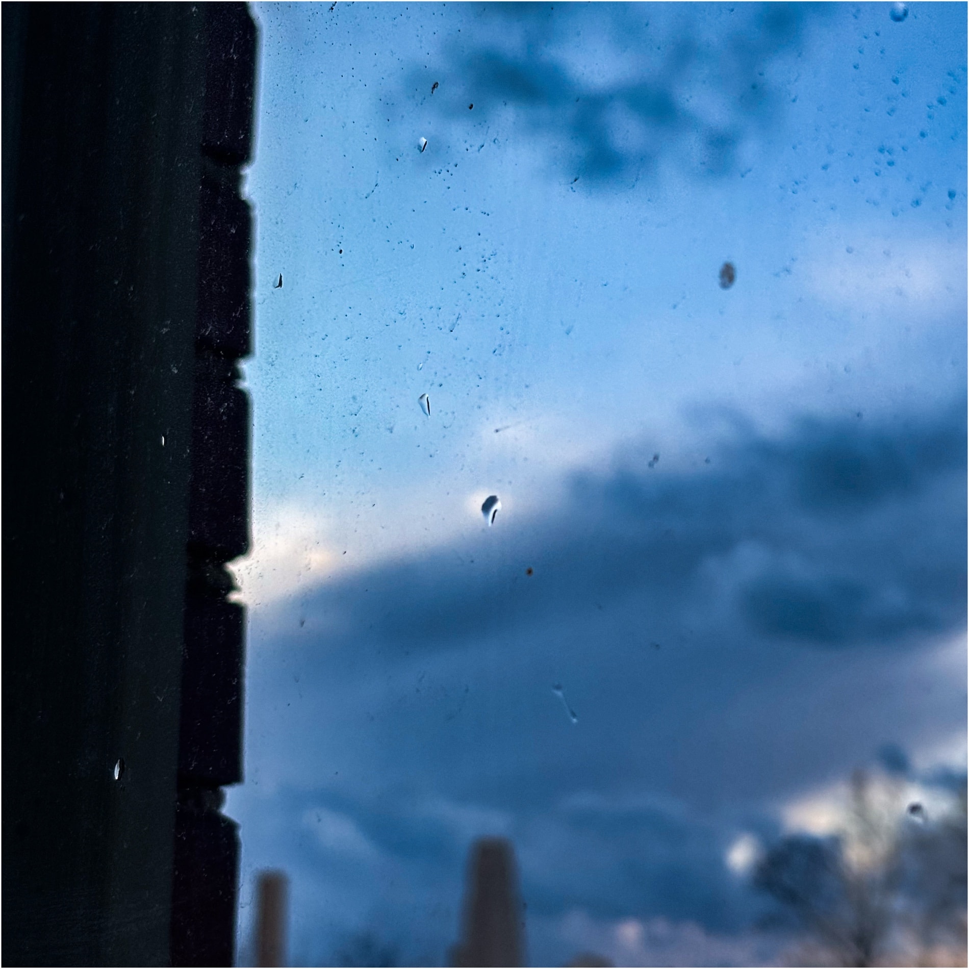 Blue hour seen through a rain-flecked window beside a dark post
