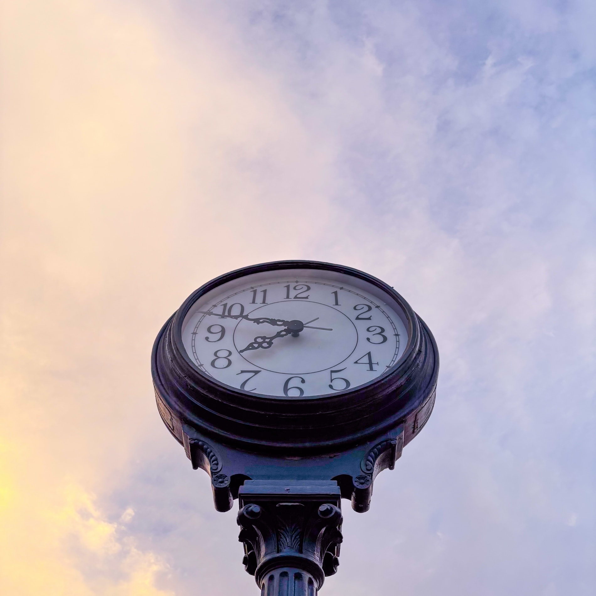 A cast-iron street clock against a lilac and gold evening sky